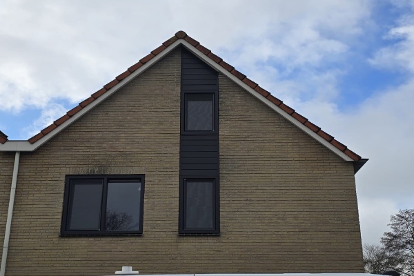 Witte kunststof kozijnen in een roodbruine bakstenen gevel met dubbele ramen en uitzicht op een groen landschap