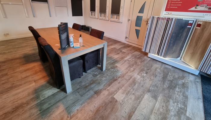 Licht grijze PVC vloer met een tafel erop en PVC stalen aan de muur erachter.